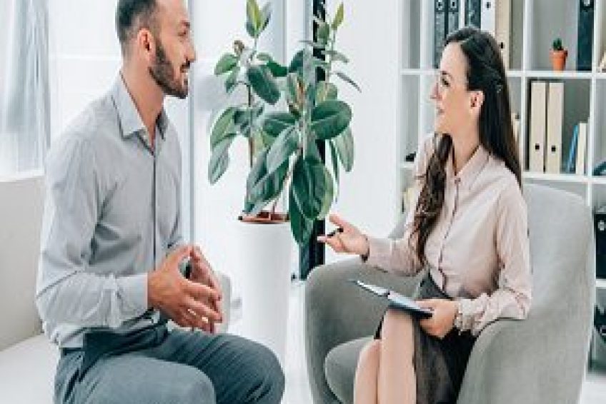 smiling psychiatrist with clipboard talking with happy patient in office